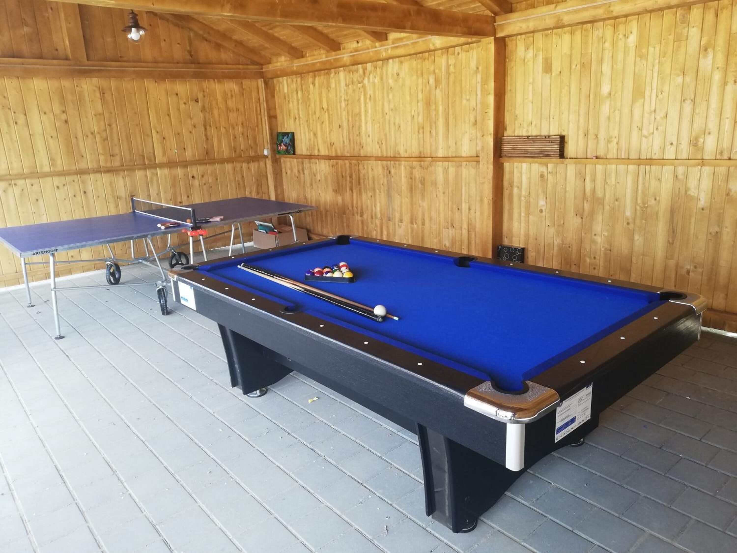 A pool table with billiard balls, a ping pong table, and a wooden wall.