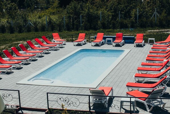 A rectangular swimming pool surrounded by red lounge chairs and white sun loungers on a tiled deck. - Popasul Montan (Avrig)
