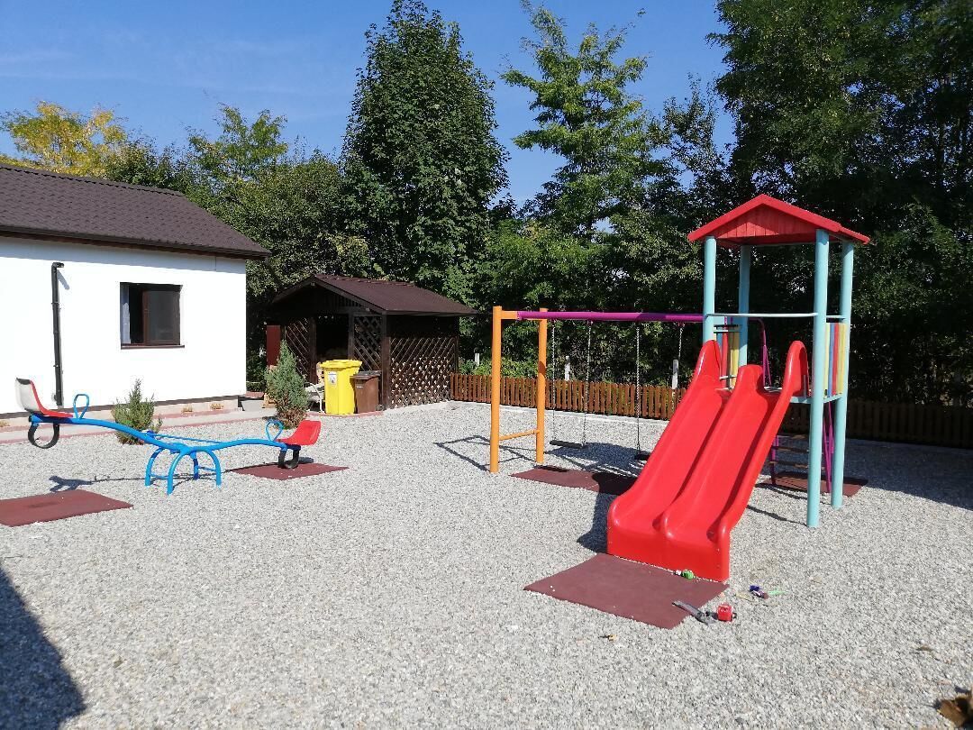 A playground with a red slide, blue seesaw, and a small shelter.