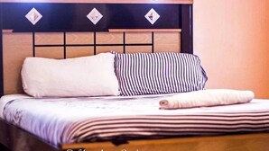 A neatly made bed with a striped pillow and a rolled towel on top. - Shamkan Lodge (Lusaka)