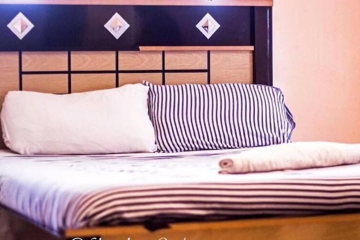 A neatly made bed with a striped pillow and a rolled towel on top.