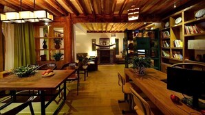 A cozy, rustic interior with wooden beams, a dining area with a fruit bowl, and a bookshelf filled with books. - Lijiang Seven Island Resort (Lijiang)