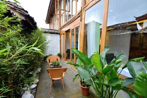 A traditional-style building with large windows, a patio area with wicker chairs and potted plants, and a stone pathway.