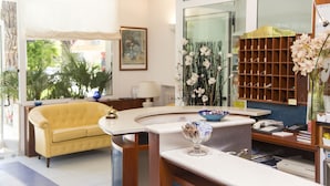 A hotel lobby with a yellow sofa, a reception desk, a glass vase with flowers, and a wooden shelf with a sign reading "Hotel Garden". - Hotel Garden Riccione (Riccione)