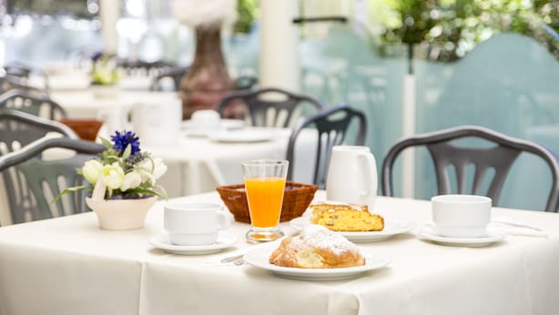 A breakfast table set with a coffee cup, a glass of orange juice, a muffin, and a small bowl of fruit. - Hotel Garden Riccione (Riccione)