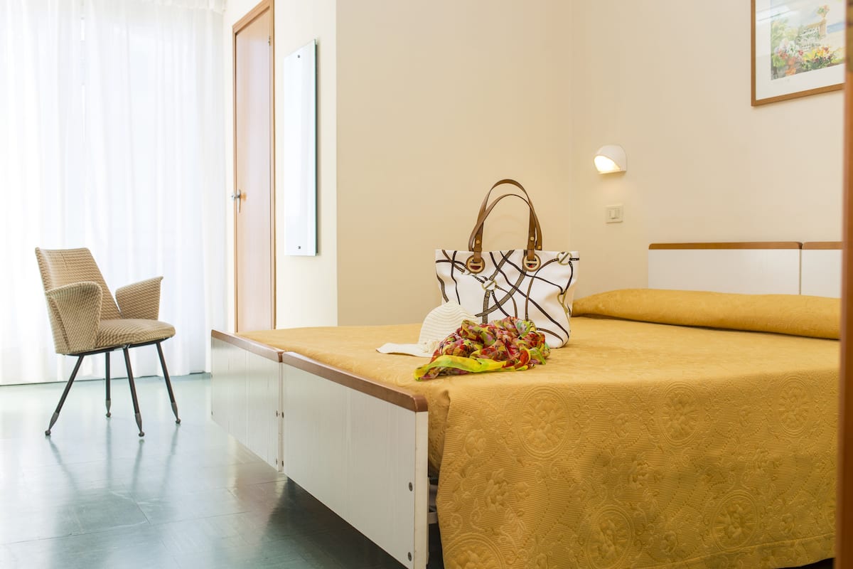 A hotel room with a bed, a chair, a wall-mounted light, and a framed picture.
