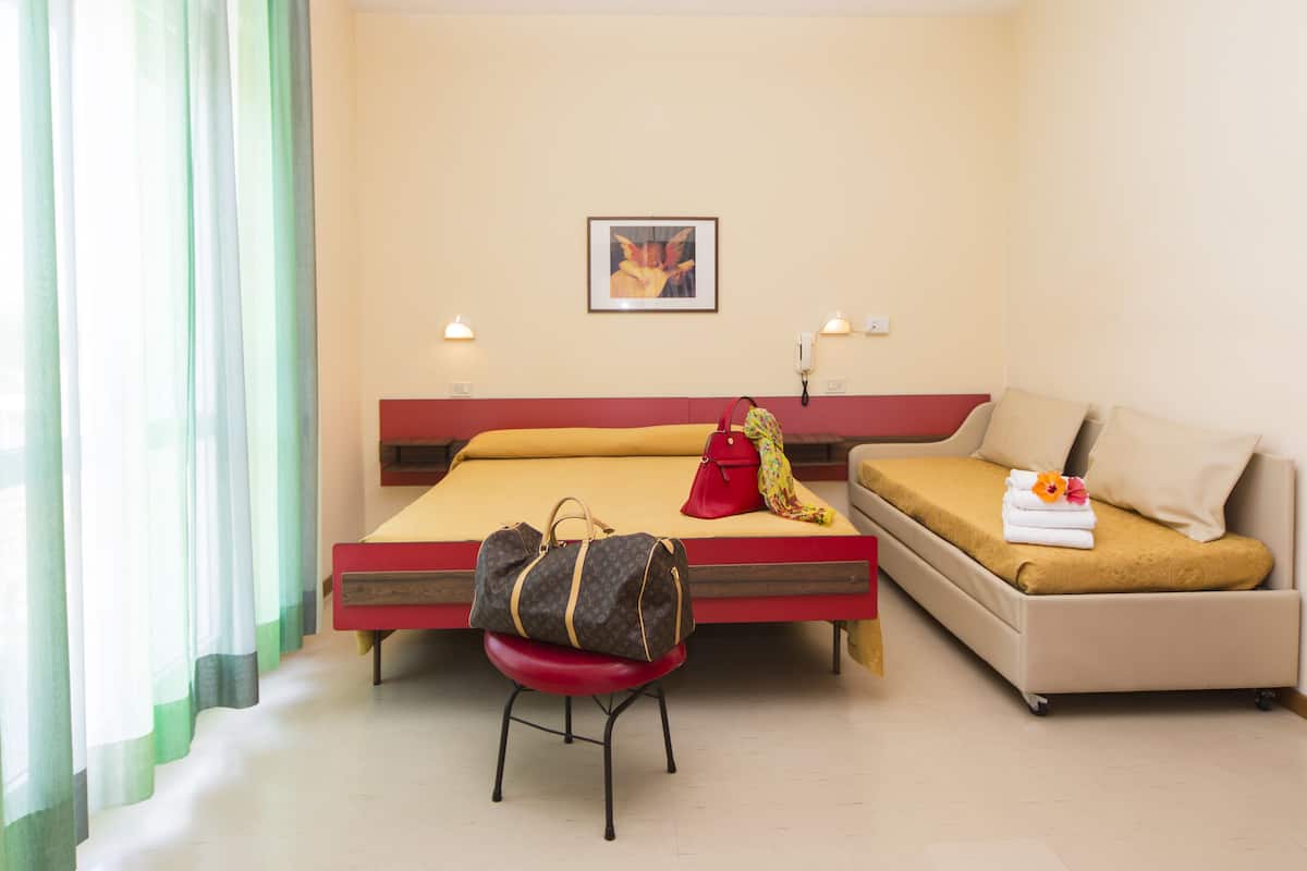 A hotel room with a bed, a sofa, a chair, and a bedside table.
