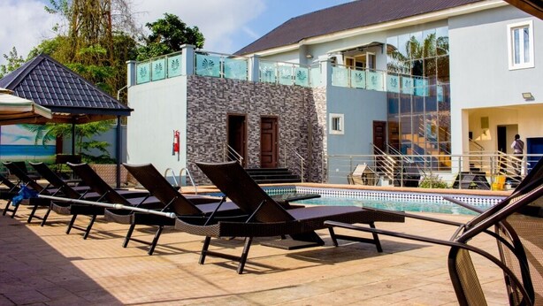 A pool area with lounge chairs, a stone wall, and a building with a balcony. - Magville Hotel (Lagos)