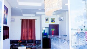 A modern living room with a chandelier, a red curtain, a television, and a bar area with a plant. - Magville Hotel (Lagos)