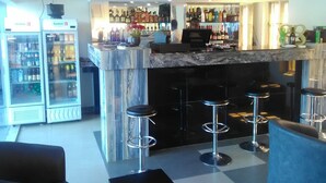A bar area with a marble counter, multiple stools, and a television screen above. - Magville Hotel (Lagos)