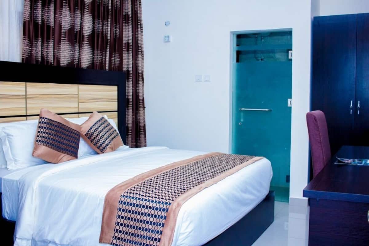 Une chambre d’hôtel avec un lit, un bureau, une armoire et une porte.