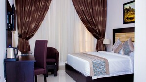 A hotel room with a bed, a chair, a desk with a kettle, and curtains. - Magville Hotel (Lagos)