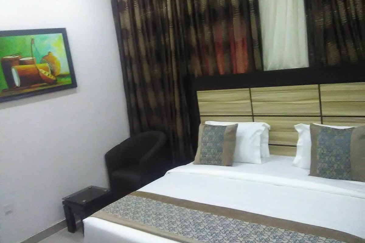 Une chambre d’hôtel avec un lit, une chaise, un tableau au mur et des rideaux.