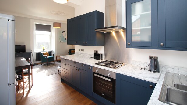 A modern kitchen with dark blue cabinets, a gas stove, and a stainless steel range hood. - Troon Golf 2024 (Troon)