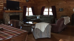 A log cabin interior with a stone fireplace, a sofa, a dining table with chairs, and mounted deer heads on the ceiling. - Cozy Quiet Cabin @ Lake Anna (Mineral)