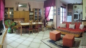 A living room with a sofa, a dining table with chairs, a TV, and a bookshelf. - B&B Fra e Fe (Arborea)