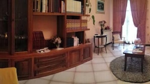 A living room with a red sofa, a wooden bookshelf, a round coffee table, and a small side table with a vase. - B&B Fra e Fe (Arborea)