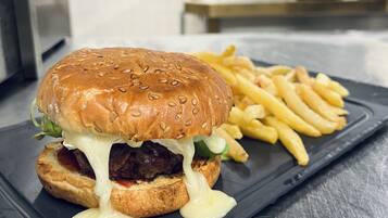 A burger with melted cheese and fries on a black plate in a kitchen setting.