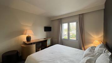 Habitación de hotel con cama, escritorio, silla, televisor y ventana con cortinas.