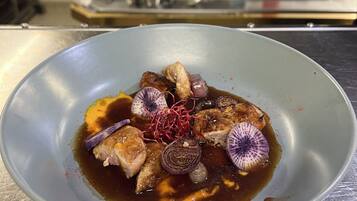 A bowl of food with a sauce, garnishes, and a kitchen in the background.