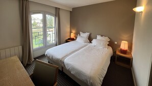 A hotel room with two beds, a desk, a chair, a window with curtains, and a view of the outside. - Le Pré Saint Germain (Louviers)