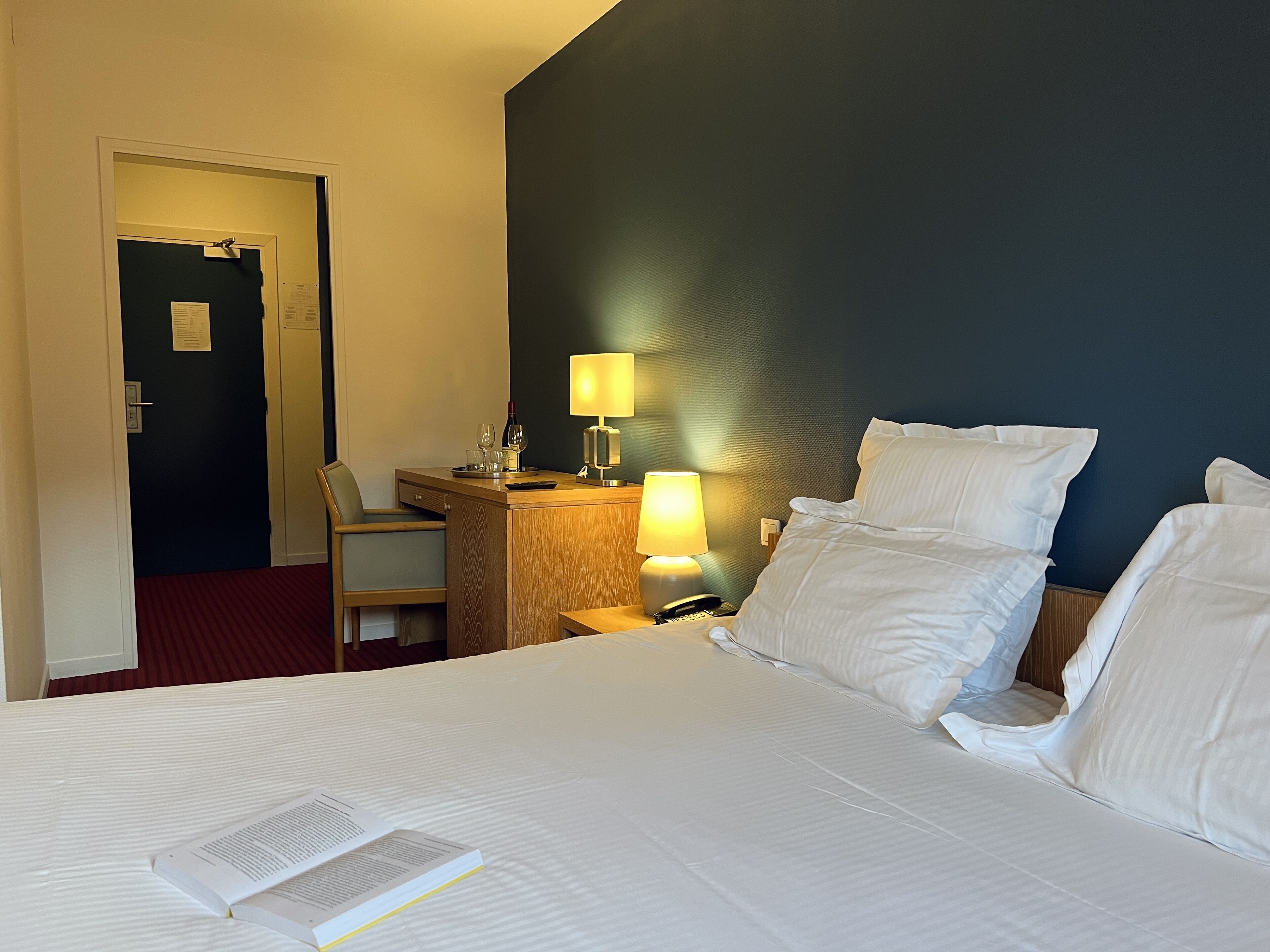 Una habitación de hotel con una cama, un escritorio con lámpara, una silla y una puerta.