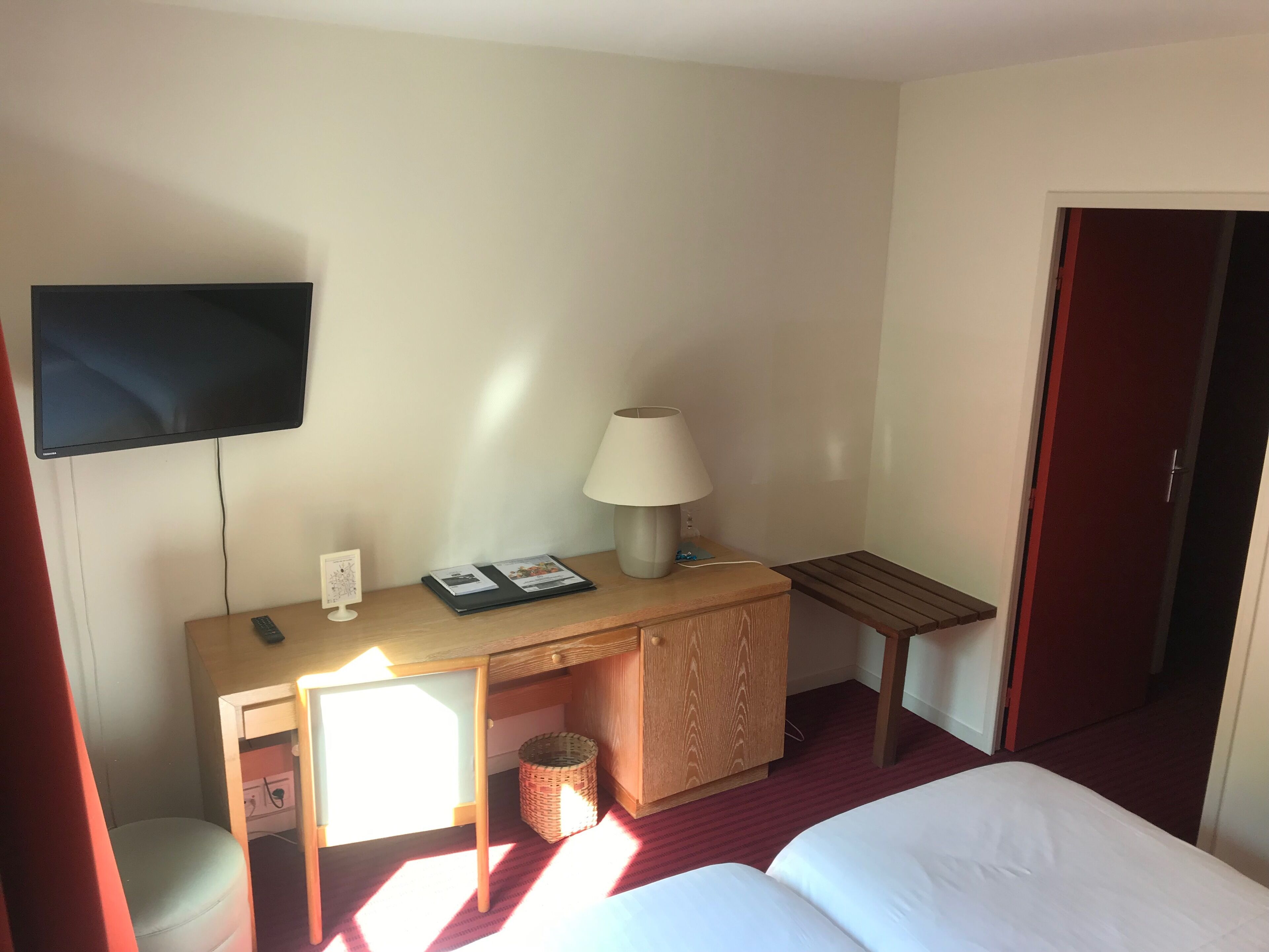 A hotel room with a bed, a desk with a lamp, a TV, and a small table.