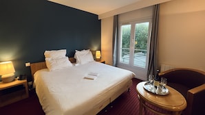 A hotel room with a large bed, two bedside tables, a small round table with a tray, and a window with a view of greenery. - Le Pré Saint Germain (Louviers)