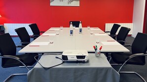 A conference room with a long table, black chairs, a projector, and a water bottle. - Le Pré Saint Germain (Louviers)