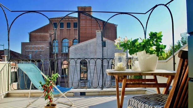 A balcony with a chair, a table with a vase and candle, and a plant. - Ca Moro - Deluxe Loft with Private Terrace (Venezia)