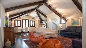 A spacious living area with a high ceiling, wooden beams, a white sofa, a blue sofa, orange bean bags, and a patterned rug. - Ca Moro - Deluxe Loft with Private Terrace (Venezia)