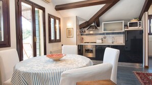 A dining area with a round table, chairs, and a bowl. There is a kitchen with appliances and a tiled backsplash. - Ca Moro - Deluxe Loft with Private Terrace (Venezia)