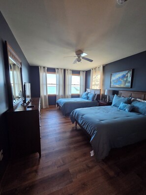 Une chambre avec deux lits, un ventilateur de plafond, un tableau et une vue sur l’extérieur.