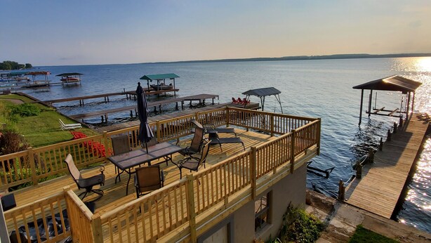 A waterfront patio with outdoor seating and a dock extending into the water. - Wine trail lakefront luxury stay on Seneca Lake with all the views and amenities (Geneva)