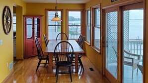 A dining area with a wooden table and chairs, a red cabinet, and a view of the water through large windows. - Wine trail lakefront luxury stay on Seneca Lake with all the views and amenities (Geneva)