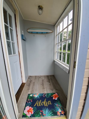 A narrow hallway with a wooden floor, a door on the left, and a window on the right.