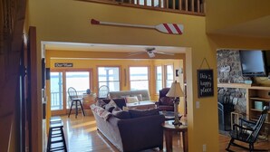 A cozy living room with a sofa, a coffee table, and a TV mounted on a stone wall. There is a sign that reads "Our Nest" and a paddle on the wall. - Wine trail lakefront luxury stay on Seneca Lake with all the views and amenities (Geneva)