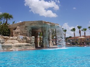 A swimming pool with a waterfall feature, surrounded by palm trees and a rocky structure. - 8926mp - Paradise Palms (Kissimmee)