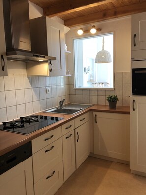 Eine moderne Küche mit weißen Schränken, einer Edelstahl-Dunstabzugshaube, einem Gasherd, einer Spüle und einem Fenster mit Außenblick.