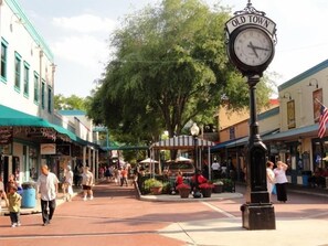 Een stadsplein met een klok waarop 'Old Town' staat, omringd door winkels en mensen.