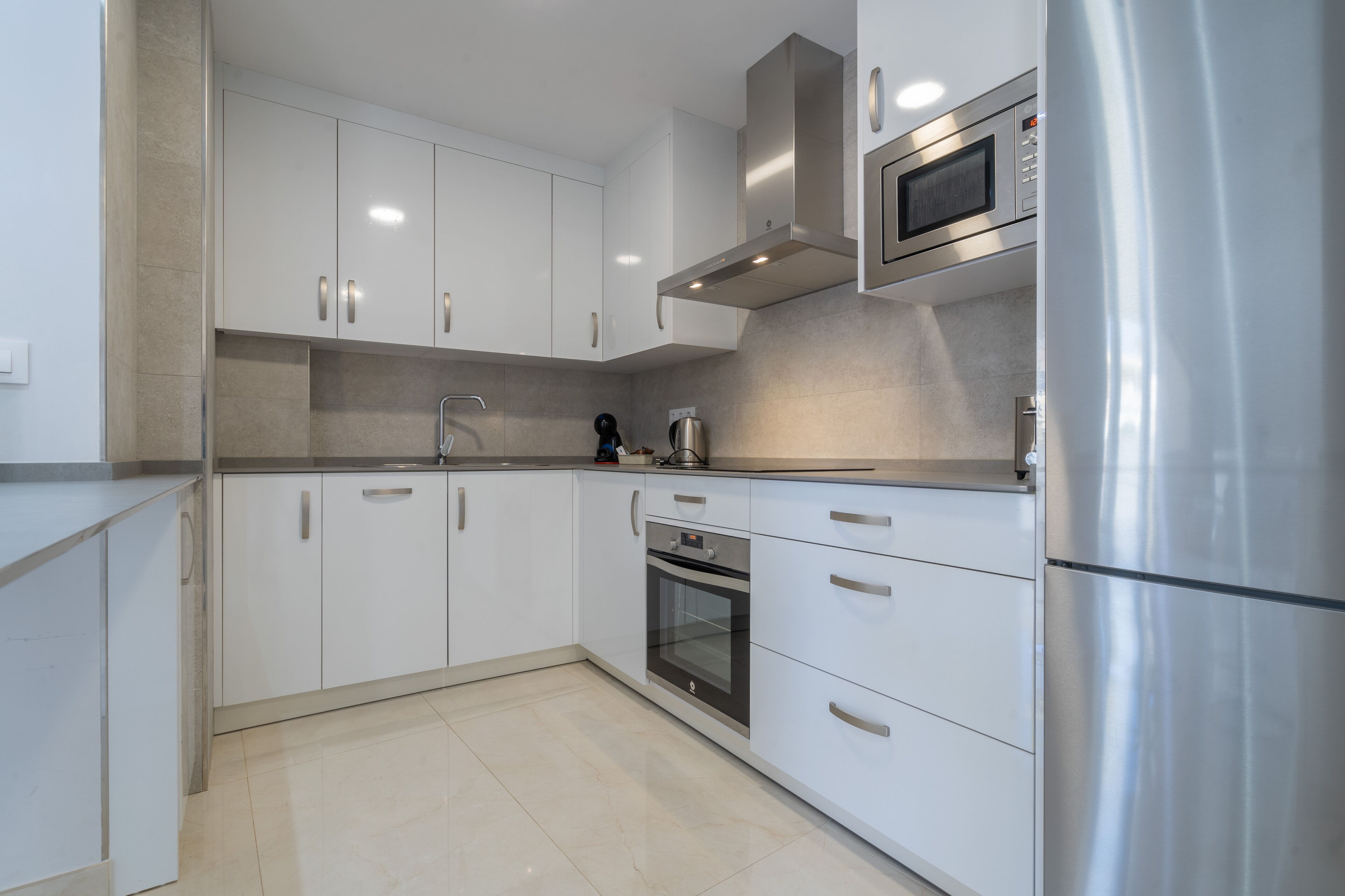 A modern kitchen with white cabinets, stainless steel appliances, and a tiled backsplash.