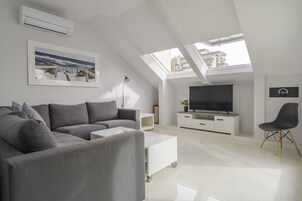 A modern living room with a grey sectional sofa, a white coffee table, a TV on a white cabinet, and a black chair.