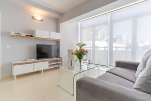 Uma sala de estar moderna com televisão de tela plana, mesa de centro de vidro e um sofá.