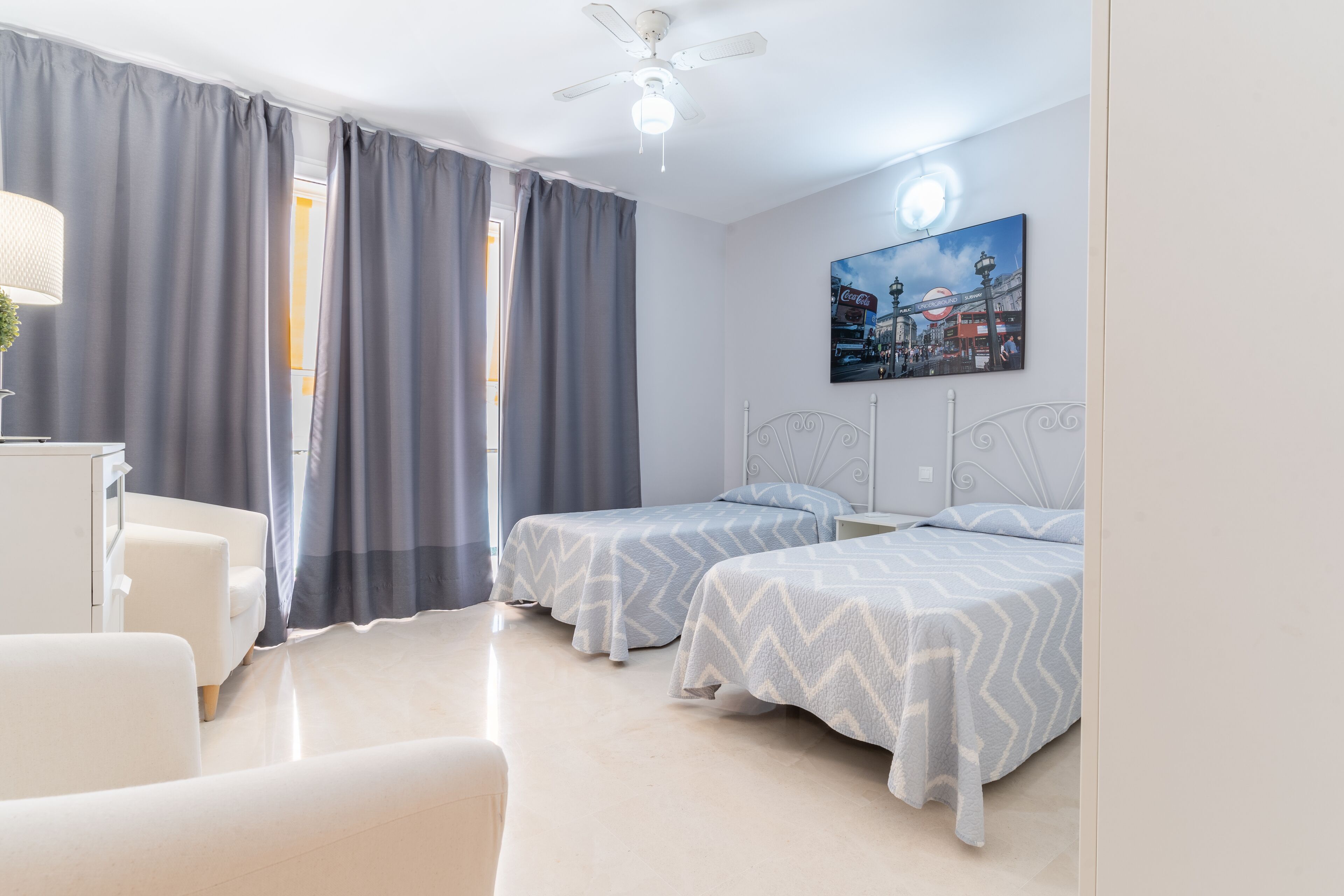 Habitació d'hotel amb dos llits, un escriptori, una cadira i un ventilador de sostre.