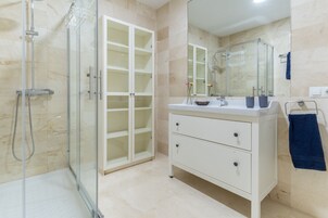 A modern bathroom with a glass shower enclosure, a white vanity with drawers, and a large mirror.