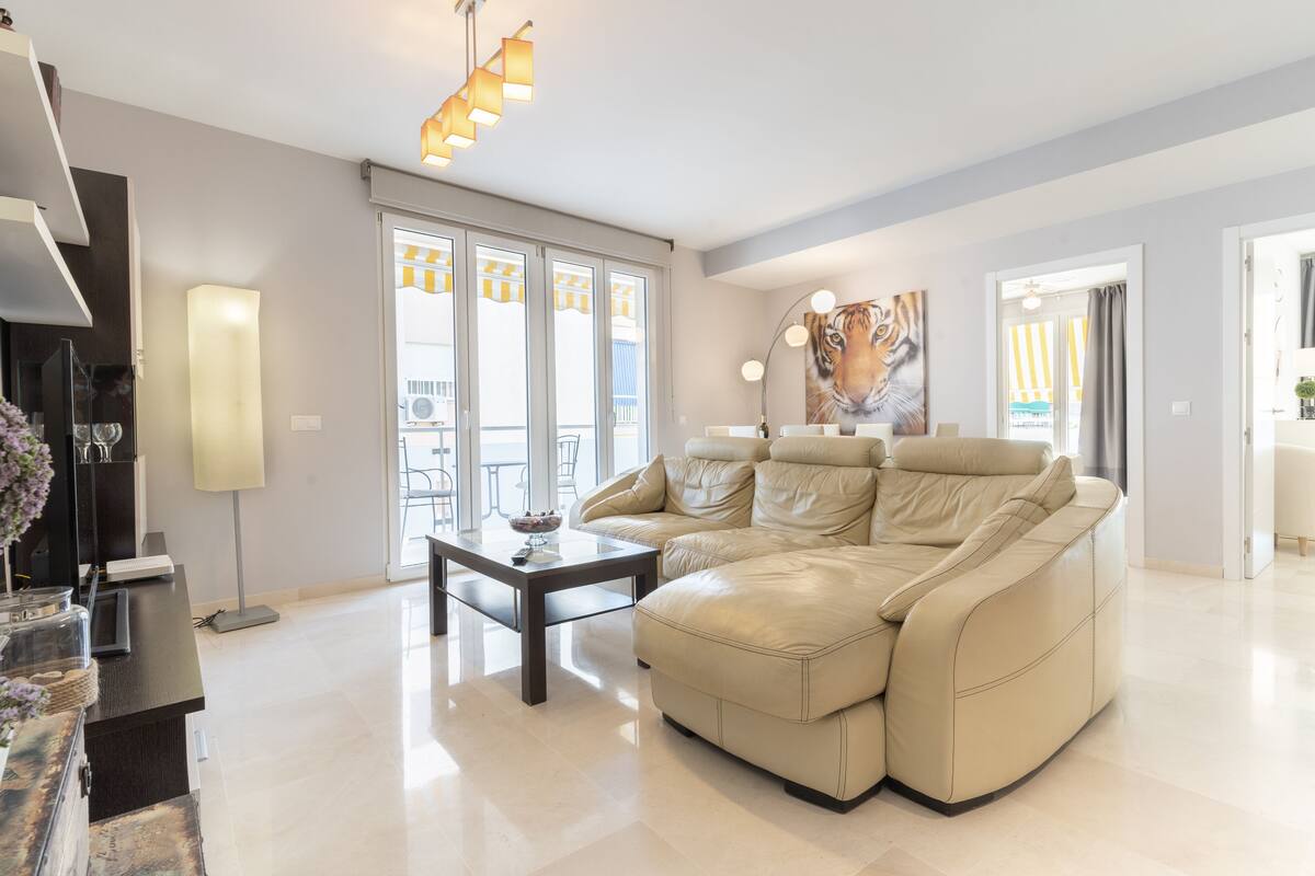 Un salon moderne avec un canapé en cuir beige, une table basse en verre et une grande fenêtre agrémentée de rideaux.