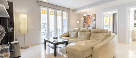 A modern living room with a beige leather sofa, a glass coffee table, and a large window with curtains.