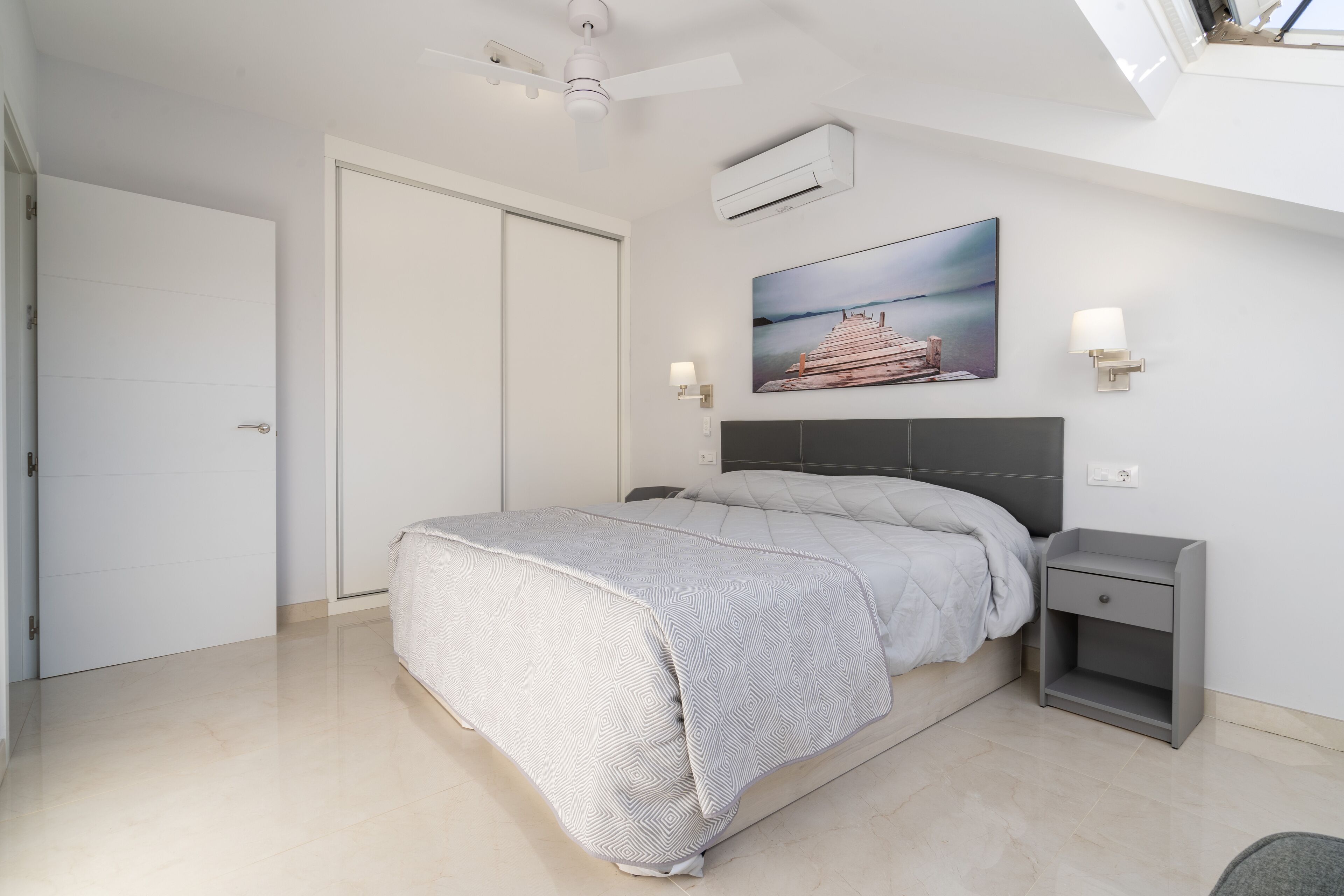 A bedroom with a bed, a nightstand, a wall-mounted lamp, and a painting.
