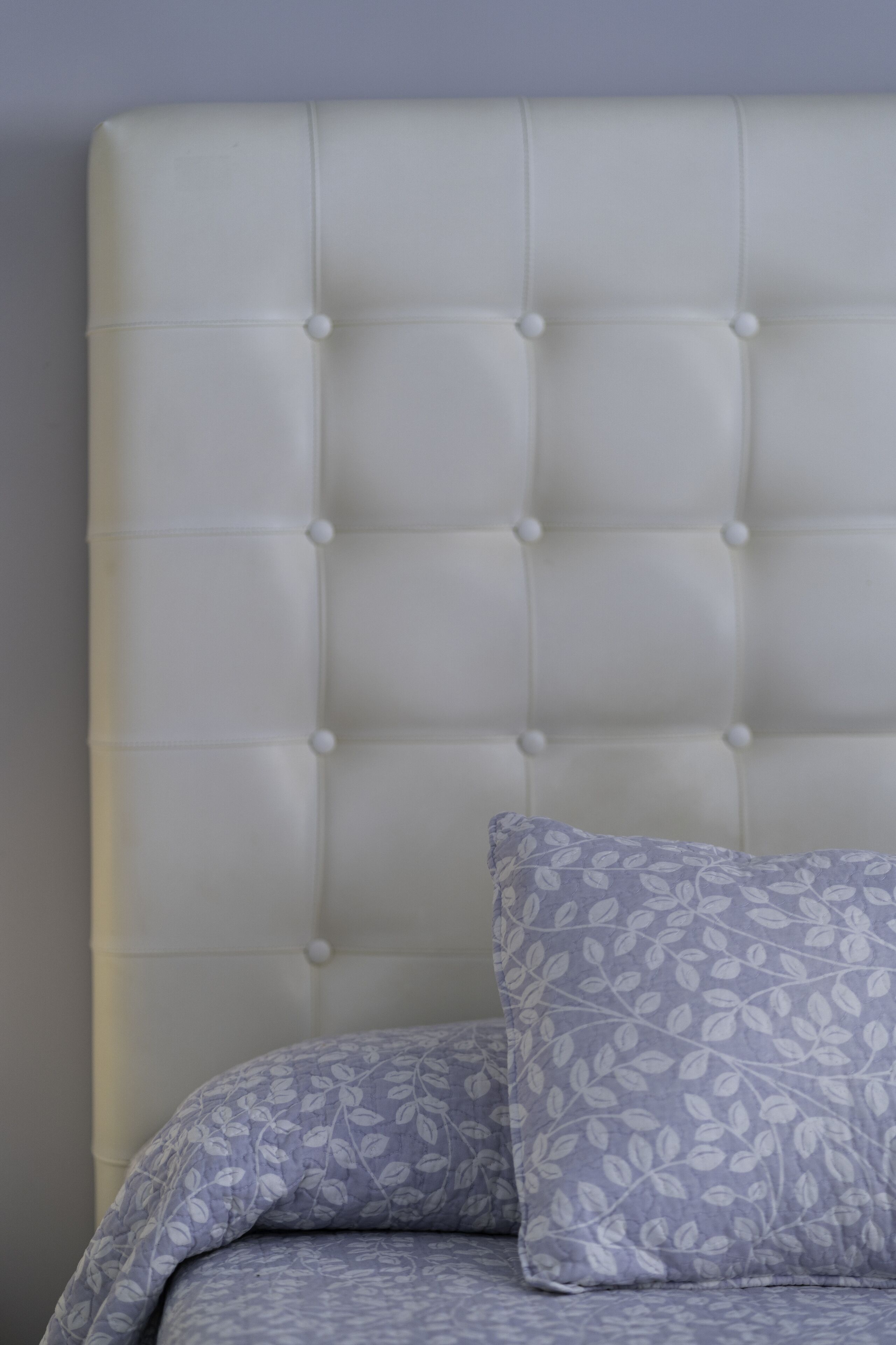A tufted headboard with a floral pillow and matching bedding.