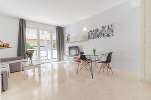 Een moderne woonkamer met een bank, een eettafel en stoelen. Er is een televisie en een plant aan de muur.